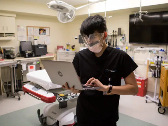 Medical scribe documenting on a laptop in an emergency department room